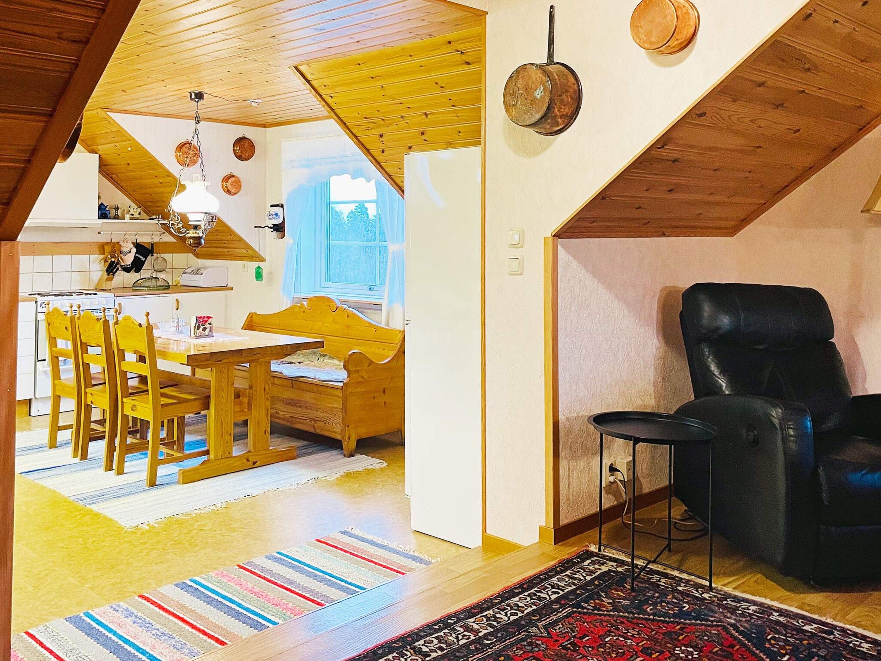 A cozy interior with a dining area, a black leather chair, and a patterned rug.