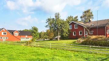 A rural landscape with a red barn, a larger red house, and a fenced field.