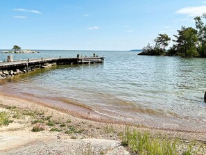 A calm lake with a wooden dock extending into the water, surrounded by a sandy shore and sparse vegetation. - 8 Person Holiday Home in Bralanda (Bralanda)