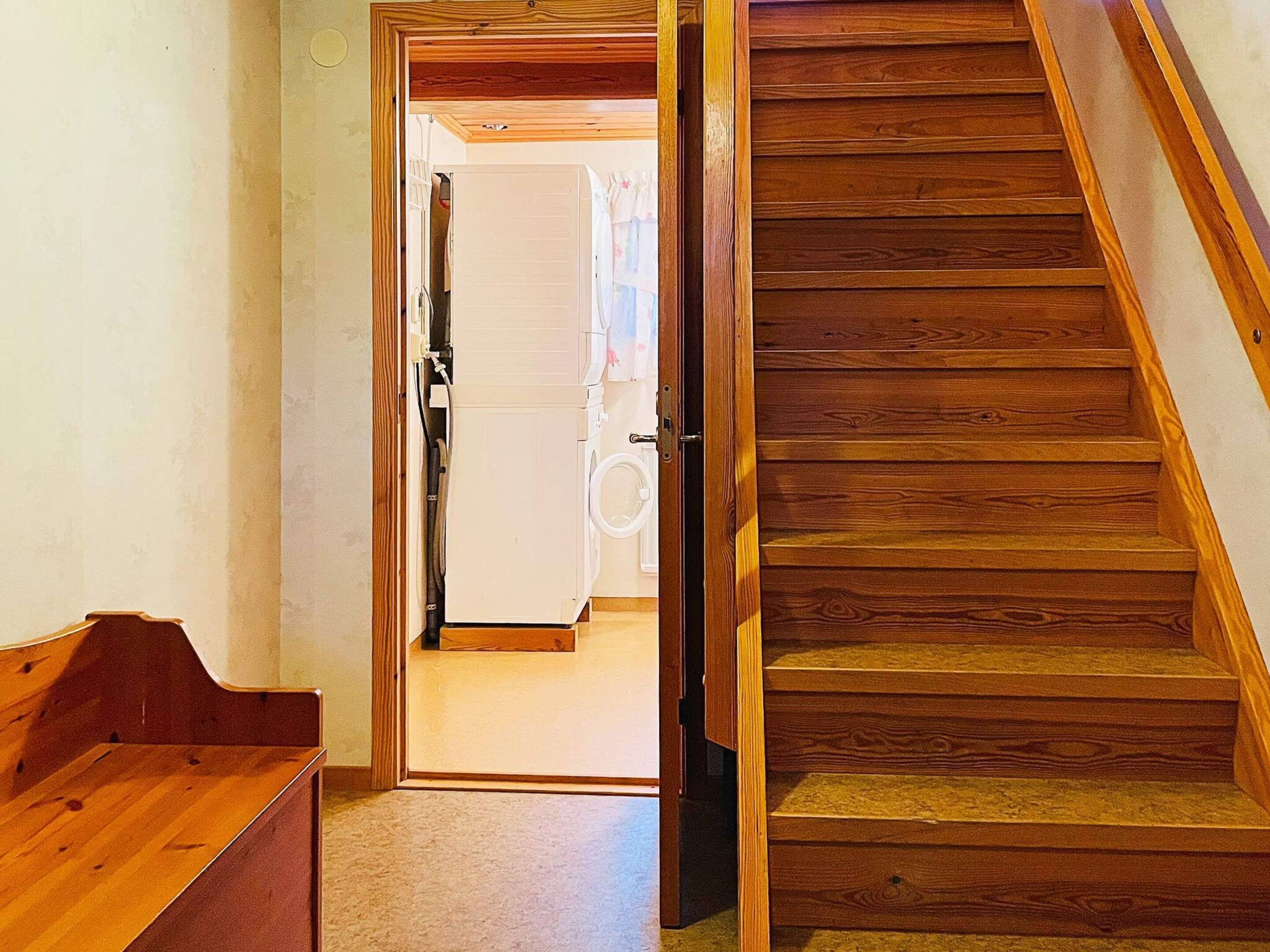 Un escalier en bois mène à une buanderie équipée d’un lave-linge et d’un sèche-linge.