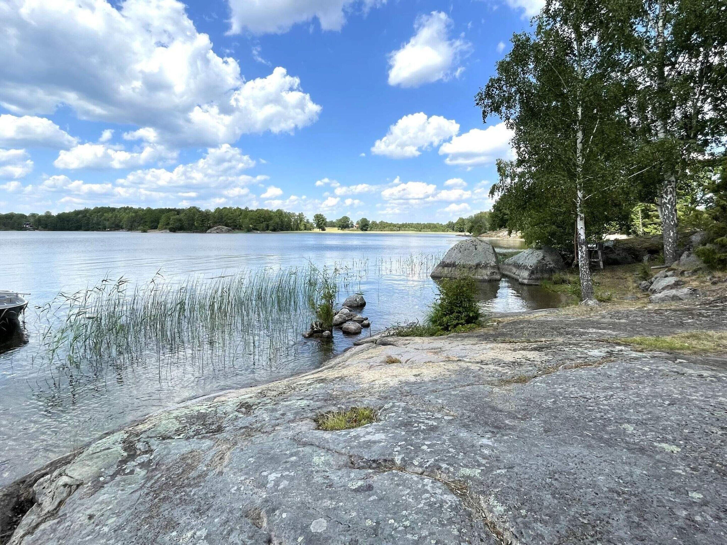 A lakeside view with calm water, rocks, and trees.