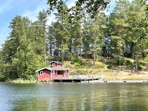 Eine rote Holzhütte mit einem Steg, der in einen See führt, umgeben von dichtem Wald.