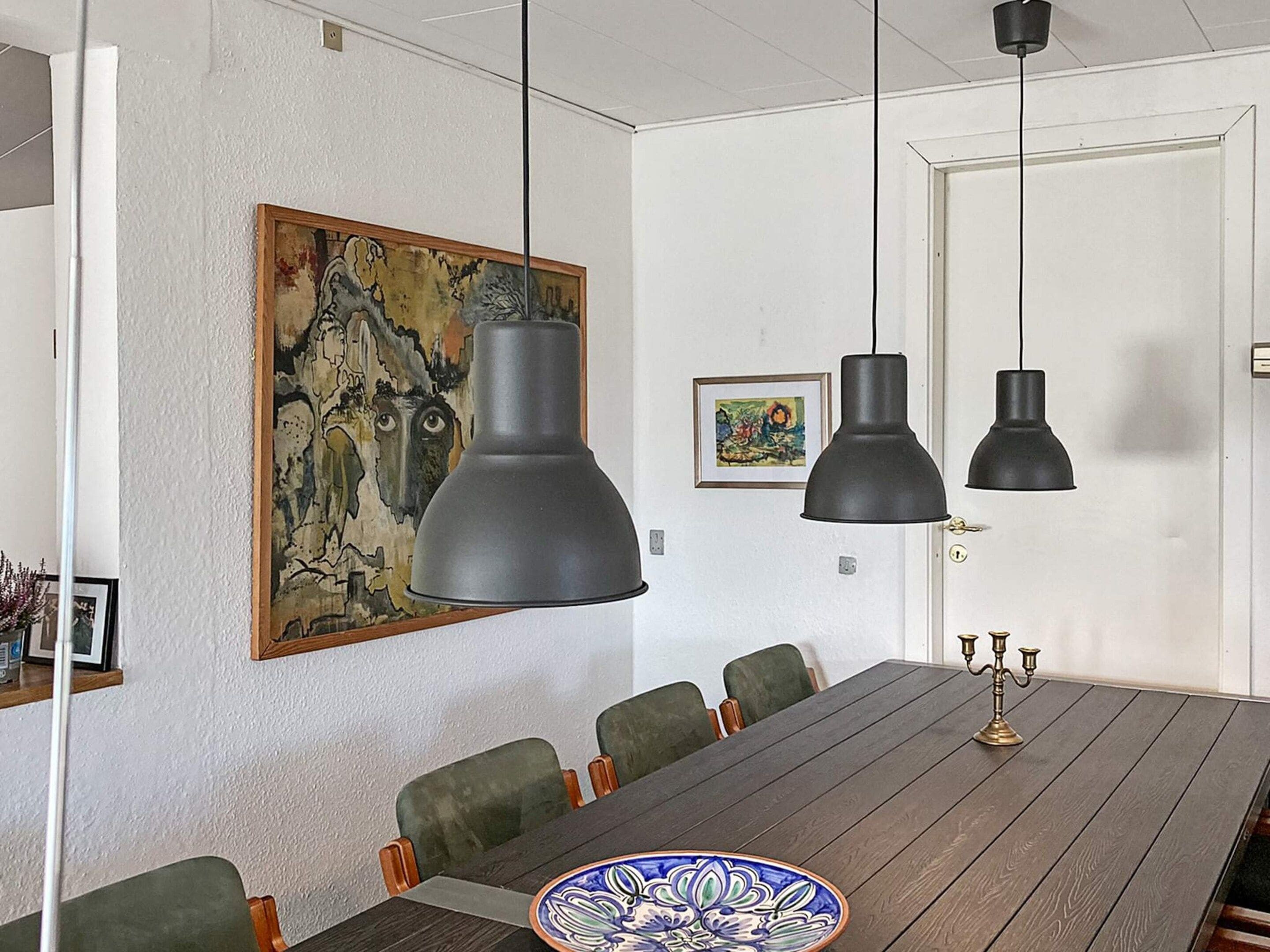 A dining area with a wooden table, green upholstered chairs, and pendant lights.