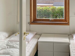 A small, compact bedroom with two beds, a window with a view of greenery, and a wooden-framed window sill. - 15 Person Holiday Home in Skibby (Skibby)
