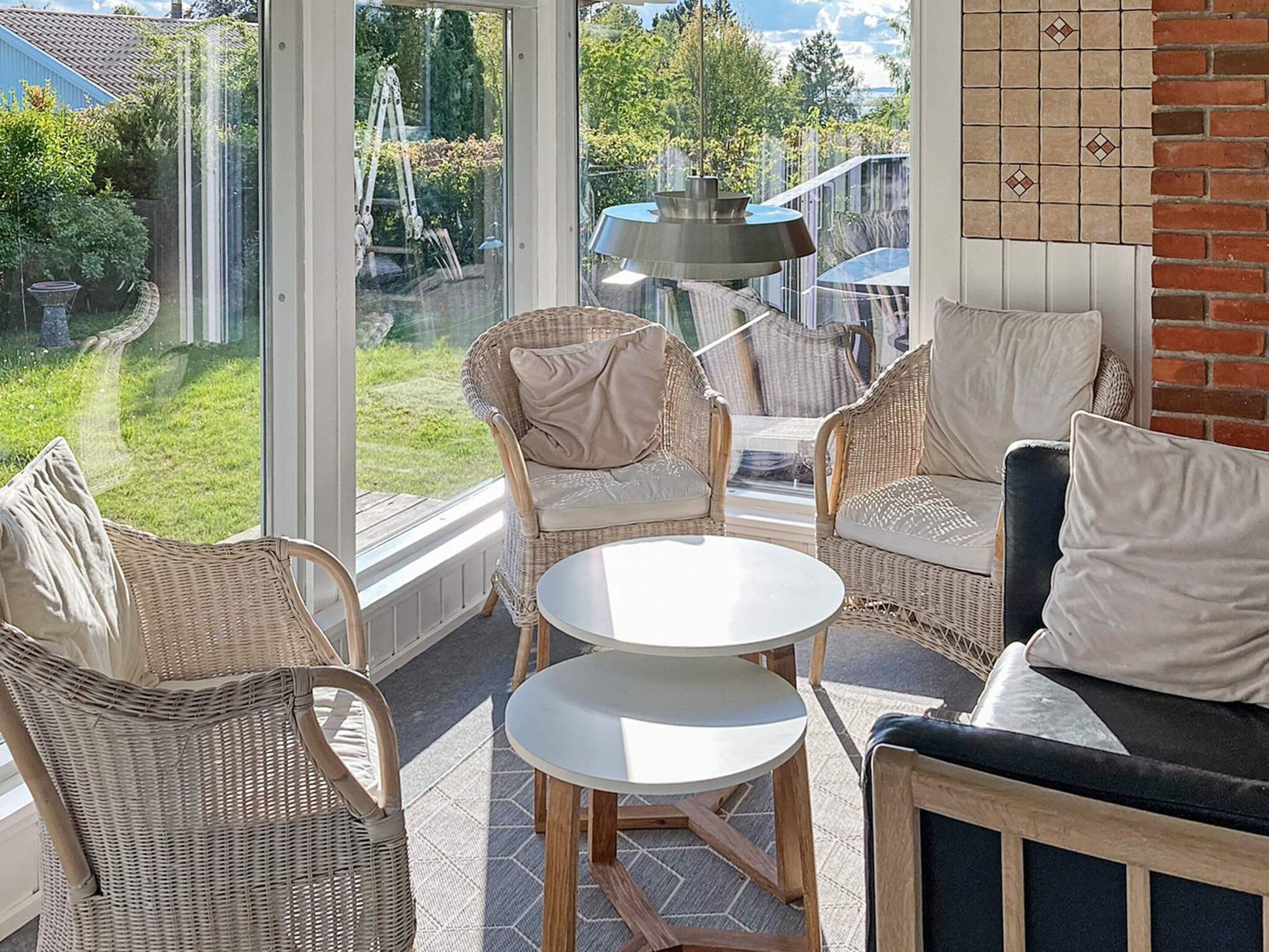 A sunlit patio with wicker furniture and a round table, overlooking a garden.
