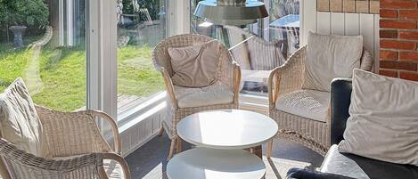 A sunlit patio with wicker furniture and a round table, overlooking a garden.