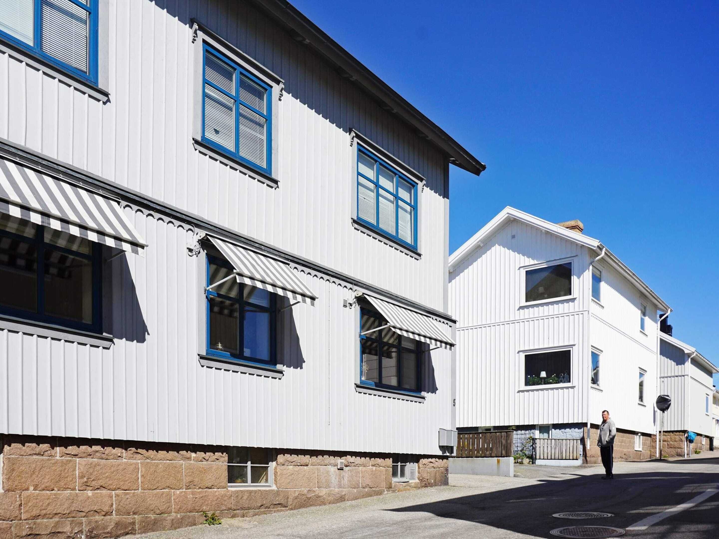 A row of white buildings with blue window frames and awnings, a clear blue sky, and a person standing on the sidewalk.
