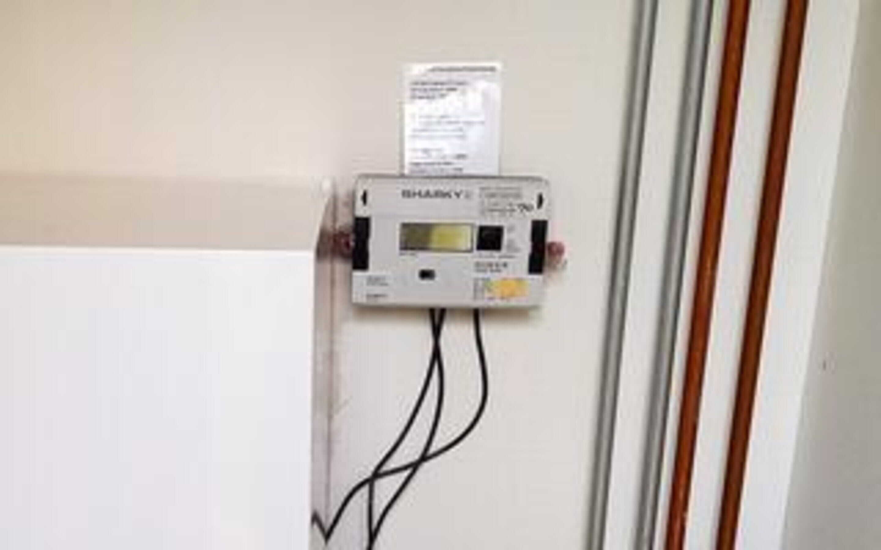 A wall-mounted electrical box with a label, two black cables, and a white door frame.