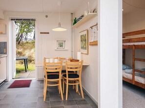 Een compacte kamer met een eettafel en stoelen, een stapelbed, een klein raam en een deur naar buiten.