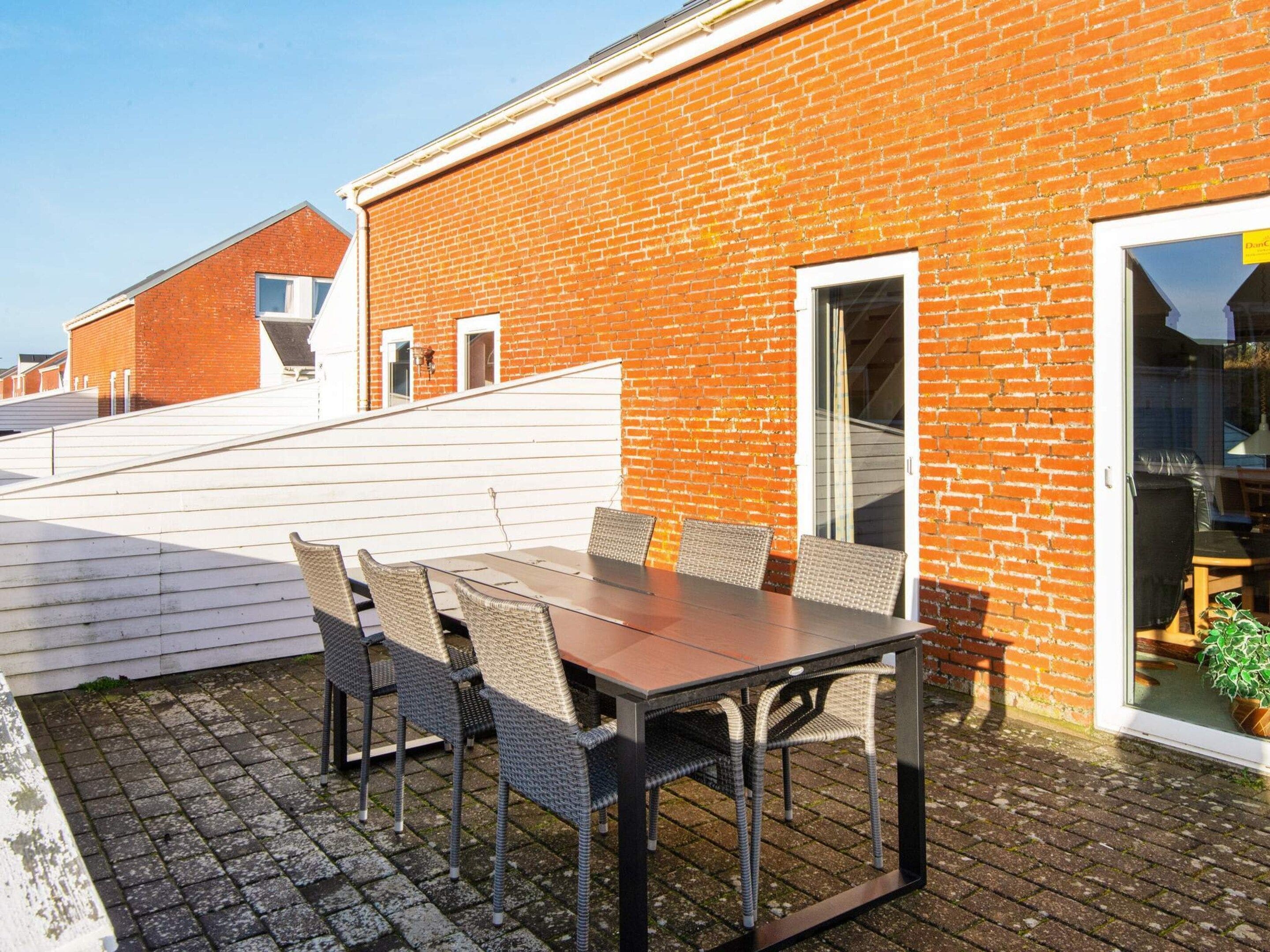 A rooftop patio with a table and chairs, a brick building, and a glass door leading inside.