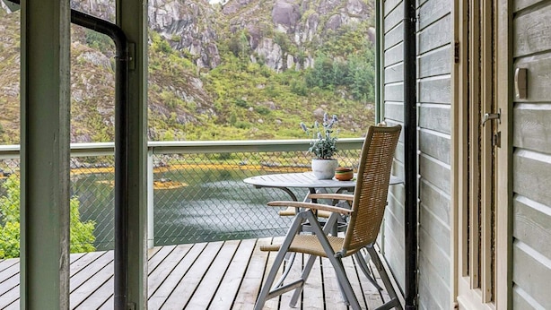Een houten terras met een tafel en een rieten stoel, met uitzicht op een rivier en een rotsachtig landschap.