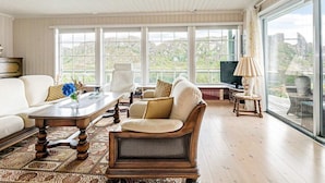 Een ruime woonkamer met een groot raam, een houten salontafel, een bank en een fauteuil.