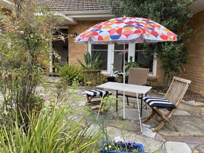 A patio with a table and chairs, surrounded by potted plants and a colorful umbrella. - Spacious and comfortable home in fantastic area (Beaumaris)
