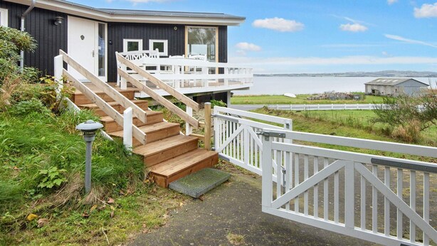 A modern house with a wooden staircase leading to a deck overlooking a body of water. - 4 Person Holiday Home in Knebel (Knebel)