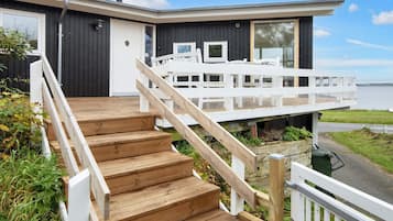 A modern house with a wooden staircase leading to a white deck overlooking a body of water.