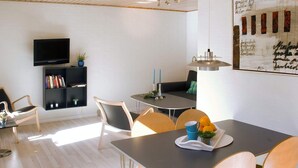 A modern living room with a flat-screen TV, a bookshelf, a dining table with chairs, and a large framed artwork on the wall. - 4 Person Holiday Home in Allinge (Allinge)