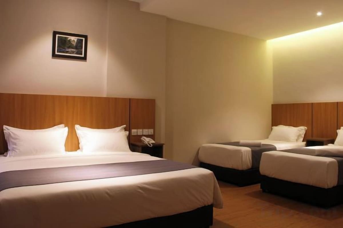 Una habitación de hotel con una cama grande, dos camas más pequeñas, una mesita de noche con lámpara y un teléfono en la pared.