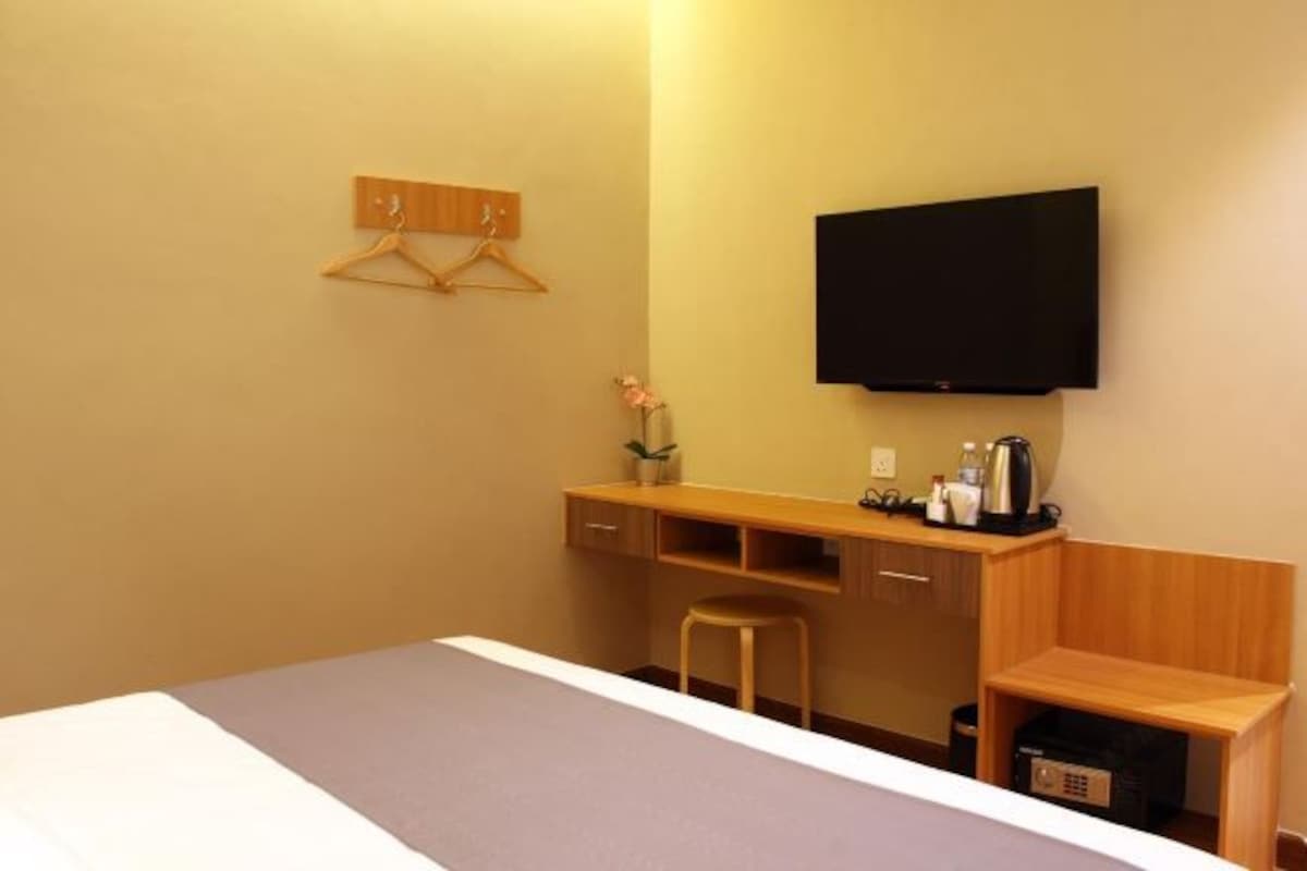 A hotel room with a bed, a desk, a chair, a TV, and a small table with a kettle and cups.