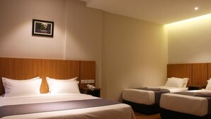 A hotel room with a large bed, two smaller beds, a bedside table with a phone, and a wall-mounted picture. - Ahyu Hotel (Kuala Lumpur)