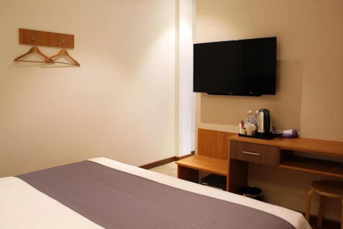 A hotel room with a bed, a wooden desk, a television, and a coat rack.