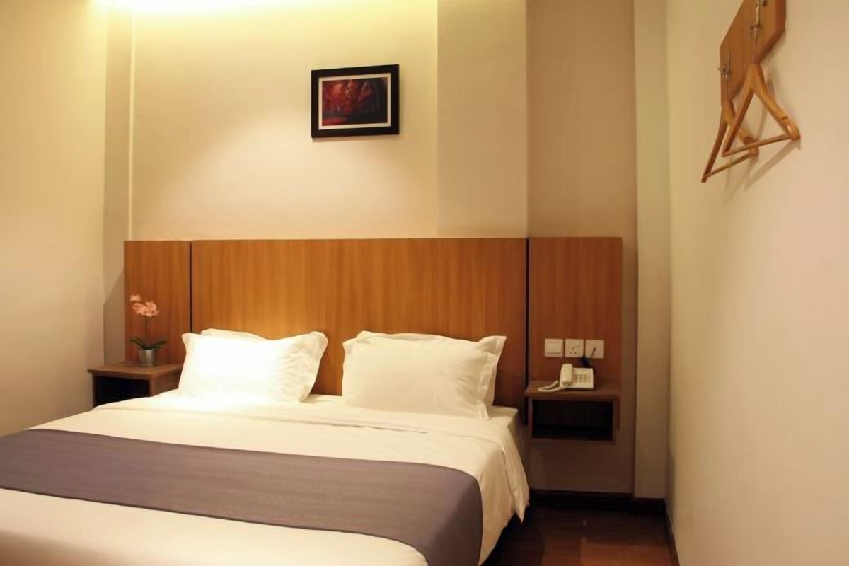 A hotel room with a bed, a nightstand, a wall-mounted telephone, and a wooden headboard.