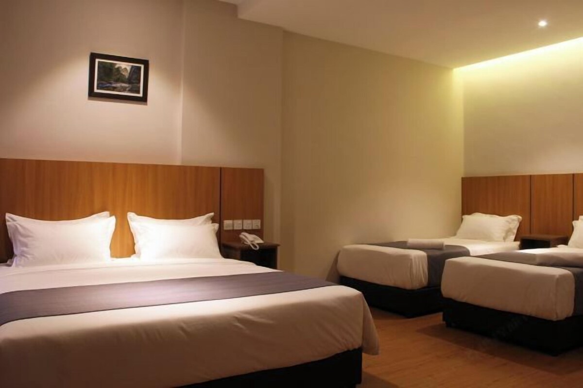 A hotel room with a large bed, two smaller beds, wooden headboards, a bedside table with a phone, and a framed picture on the wall.