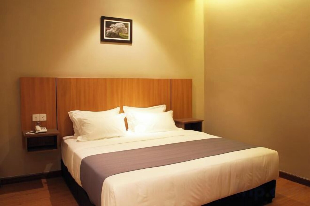 A hotel room with a large bed, a nightstand, a bedside table, and a wall-mounted picture.
