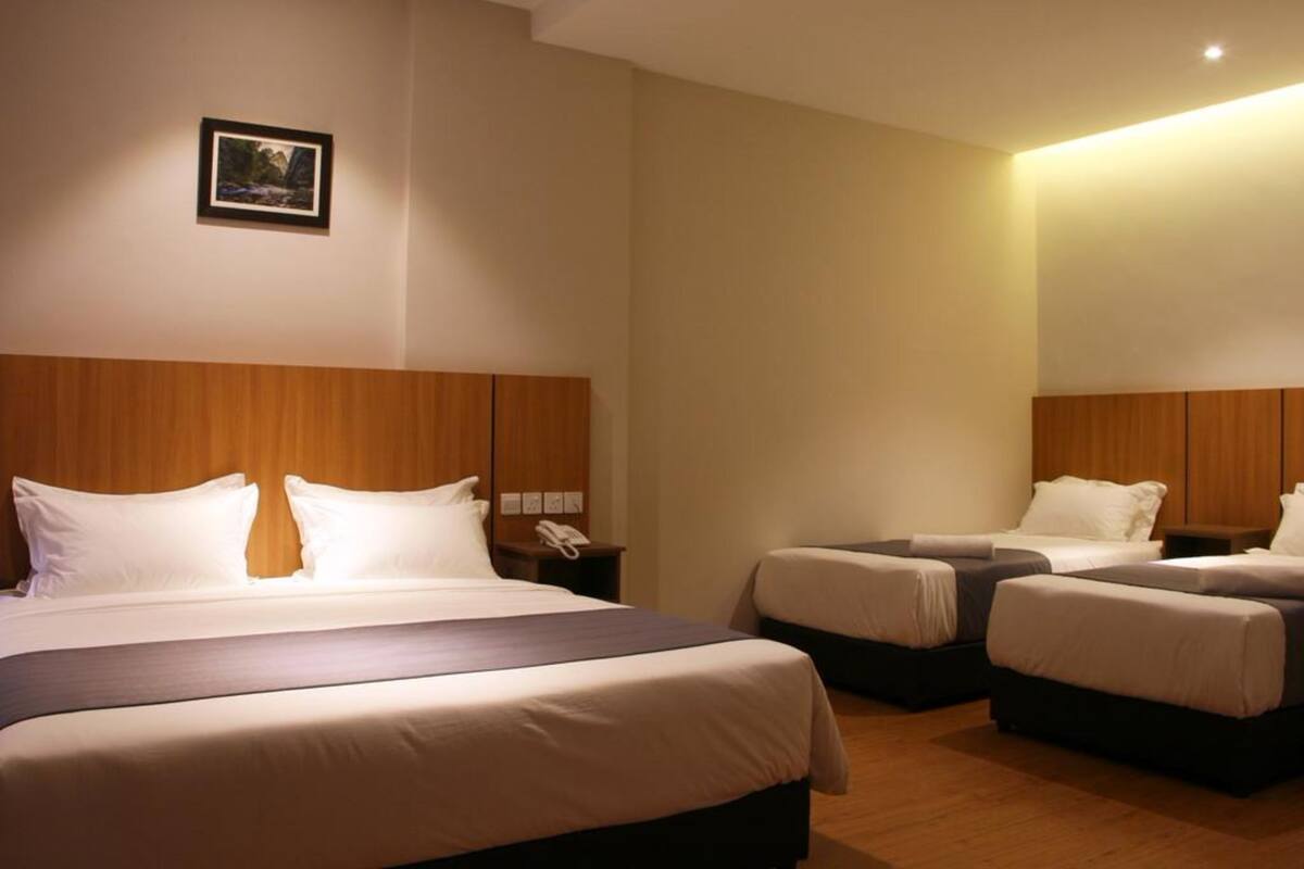 A hotel room with a large bed, two smaller beds, wooden headboards, a bedside telephone, and a framed picture on the wall.