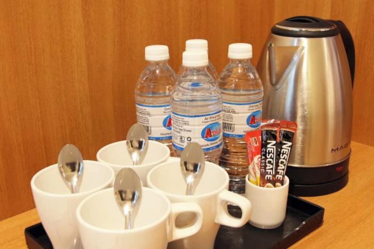 A tray with four white cups, two spoons, three water bottles, a Nescafé coffee maker, and a packet of Nescafé coffee.