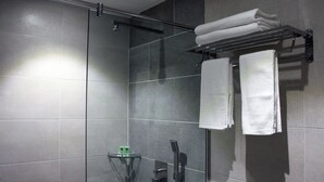 A modern shower area with a glass-enclosed shower, a towel rack with folded towels, and a small shelf with toiletries. - Ahyu Hotel (Kuala Lumpur)