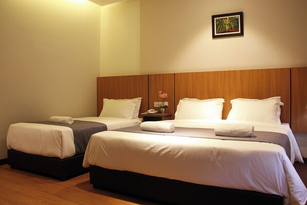 A hotel room with two beds, a wooden headboard, a small table with a vase of flowers, and a framed picture on the wall. - Ahyu Hotel (Kuala Lumpur)