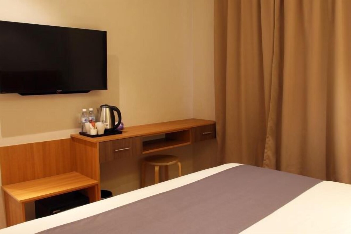 A hotel room with a bed, a desk, a chair, a television, and a coffee maker.