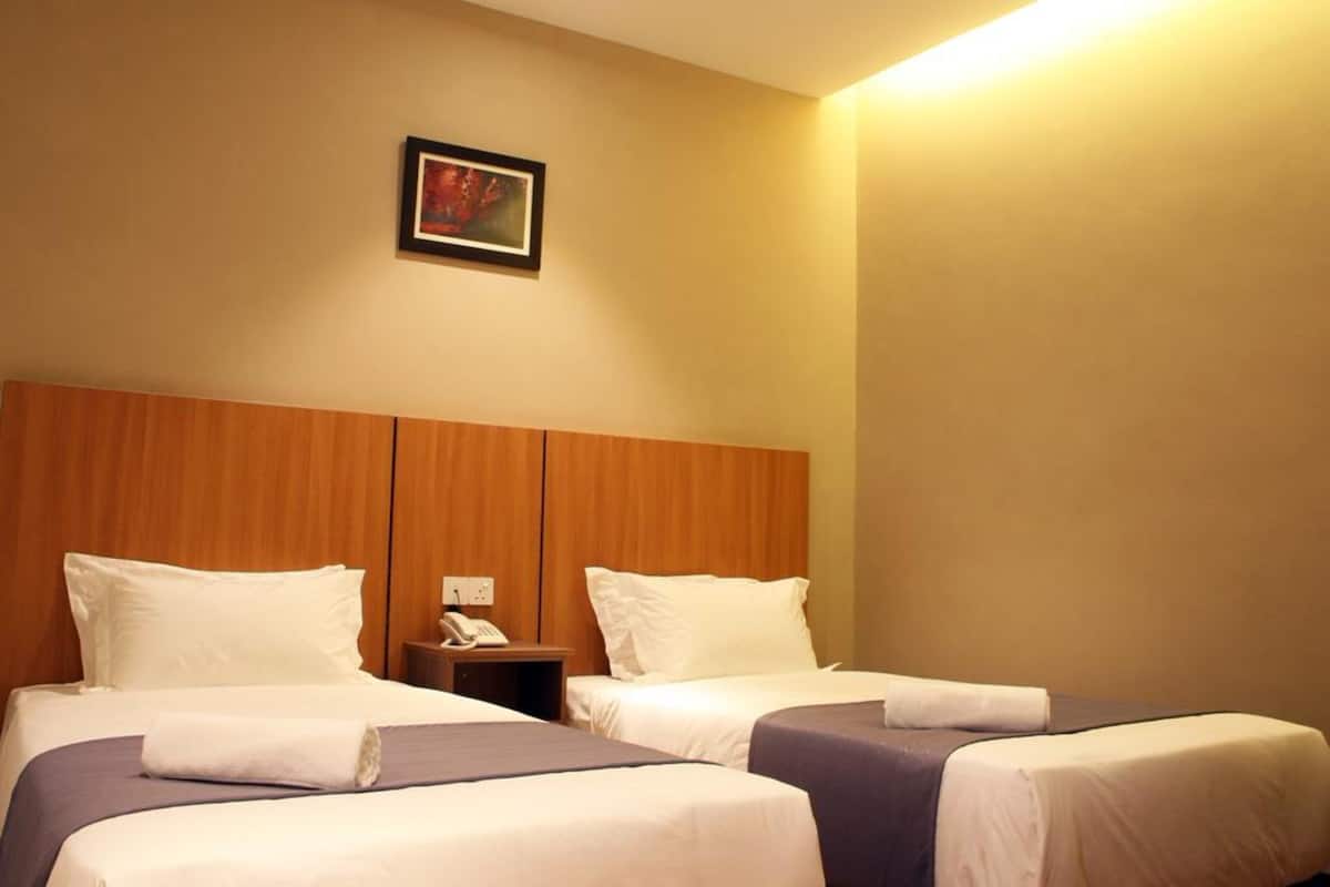 A hotel room with two beds, a wooden headboard, a bedside table with a phone, and a framed picture on the wall.