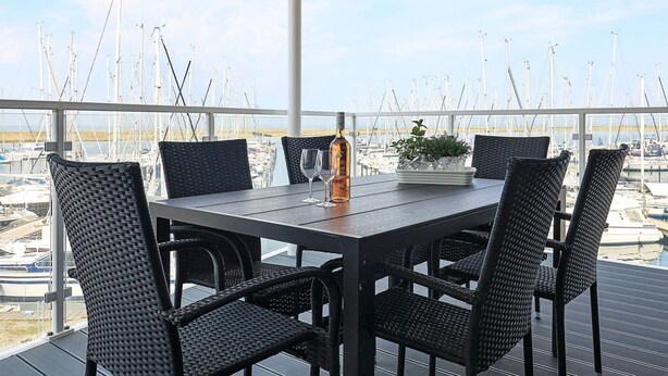 A terrace with a table and chairs, overlooking a marina with numerous boats.