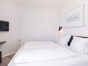Ein modernes Schlafzimmer mit einem großen Bett, einem an der Wand montierten Fernseher und einem gerahmten Zitat an der Wand.