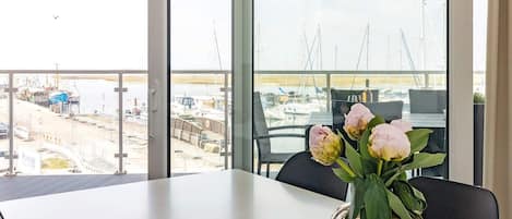 A table with a vase of flowers, a view of a marina with boats, and a modern interior design.