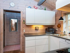 A kitchen with wooden walls, white cabinets, a clock, and a small window. - 4 Person Holiday Home in Glesborg (Glesborg)
