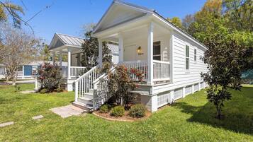 A two-story white house with a covered porch, a front yard with grass and small trees, and a visible staircase leading to the entrance.