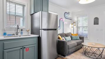 A modern kitchen with a stainless steel refrigerator, a built-in sink, and a grey sofa with colorful cushions.