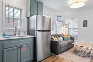 Eine moderne Küche mit einem Edelstahlkühlschrank, einer eingebauten Spüle und einem grauen Sofa mit bunten Kissen.