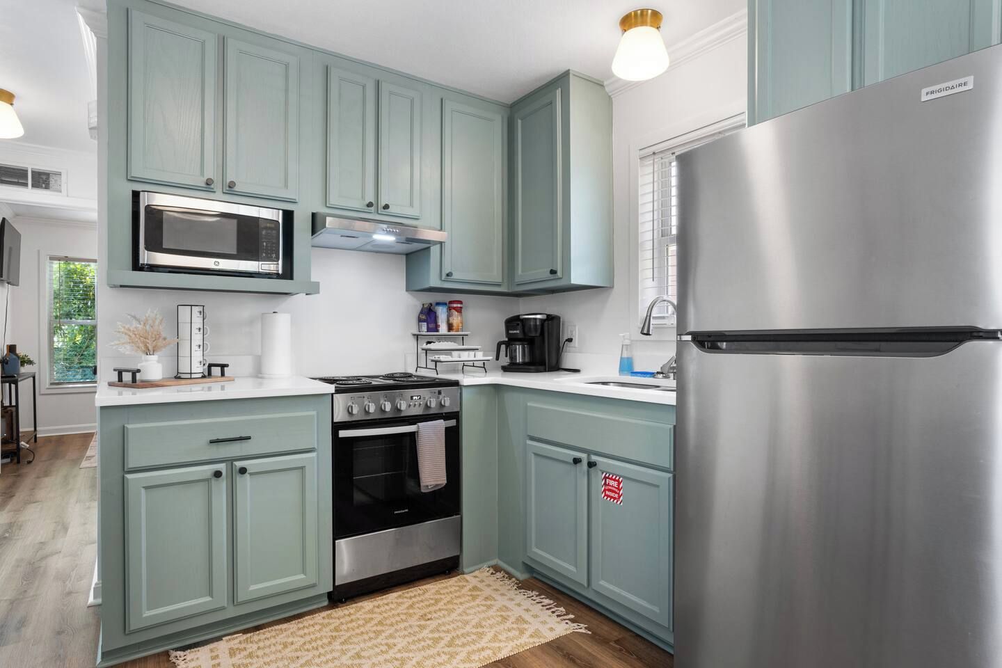 A kitchen with teal cabinets, a stainless steel refrigerator, a microwave, a stove, and a coffee maker.