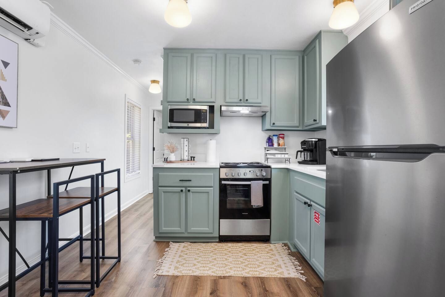 Une cuisine compacte avec des meubles de couleur turquoise, un réfrigérateur en acier inoxydable, un four à micro-ondes et une cuisinière.