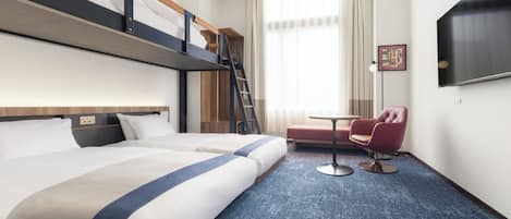 A hotel room with two beds, a bunk bed, a desk, a chair, a TV, and a window with curtains.