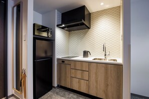 A compact kitchen with a black refrigerator, wooden cabinets, a stainless steel sink, and a hexagonal patterned backsplash.
