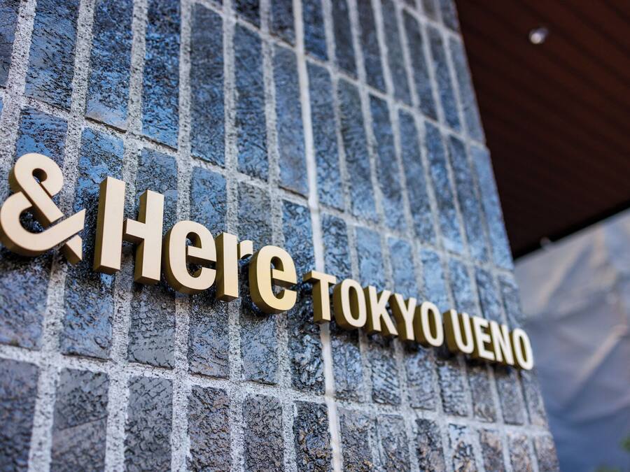 Un letrero con '&Here TOKYO UENO' en una pared texturizada.