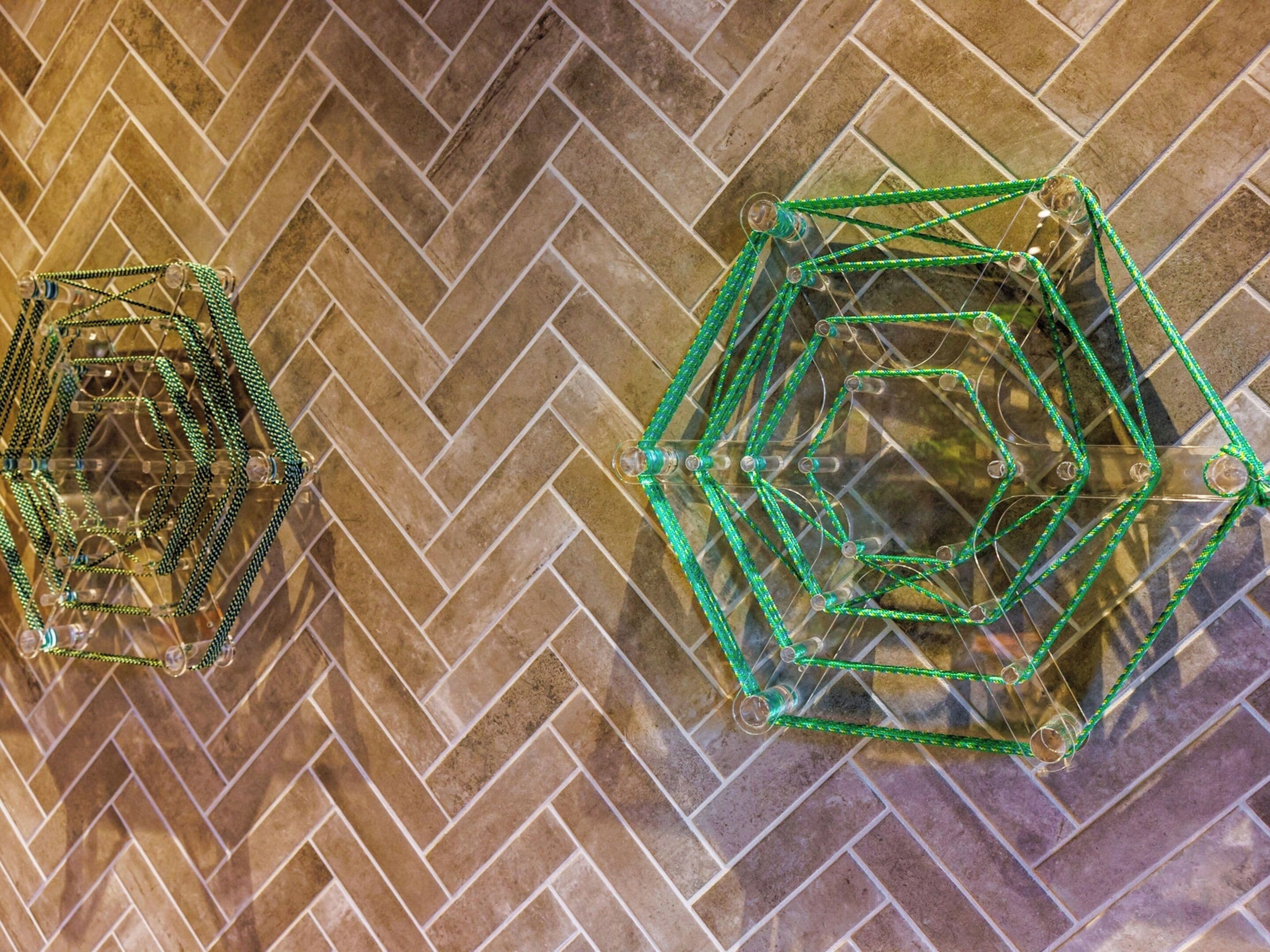 Two geometric wireframe structures on a herringbone-patterned floor.