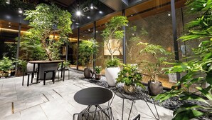 A modern indoor garden with potted plants, a dining area with a round table and chairs, and a seating area with a metal chair. - &Here TOKYO UENO (Tokyo)