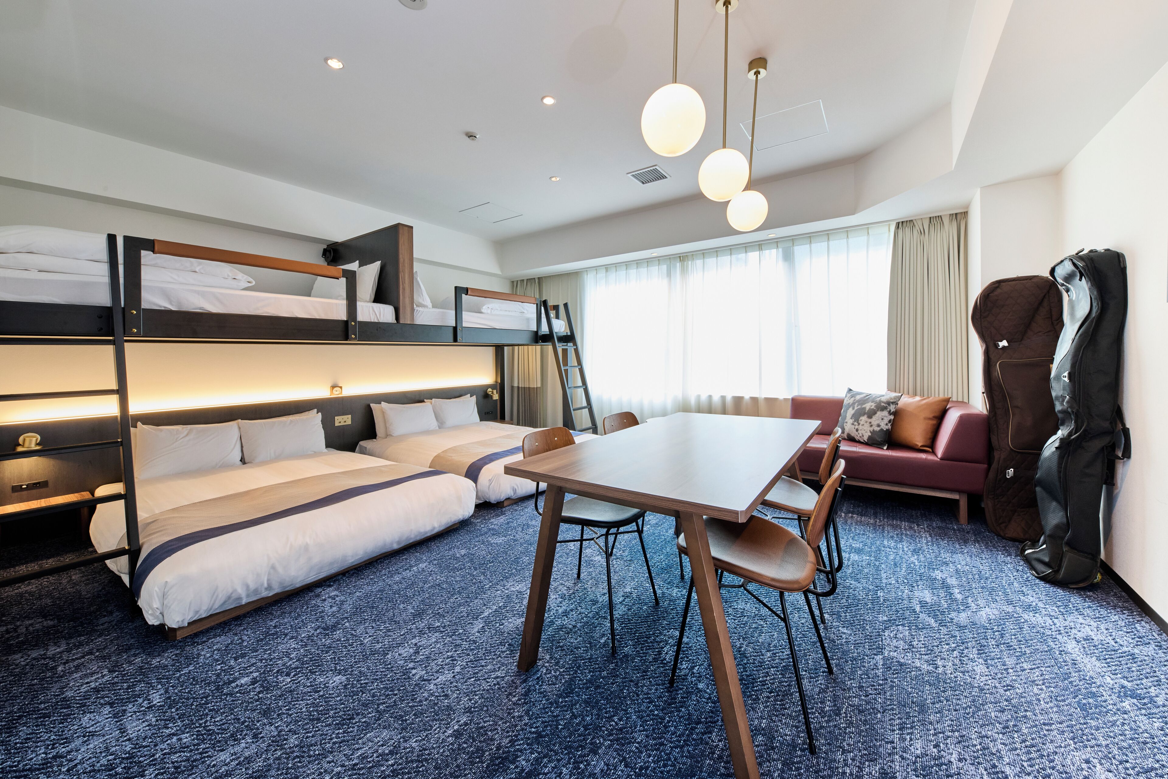 A bunk bed room with a table and chairs, a sofa, and a guitar against the wall.