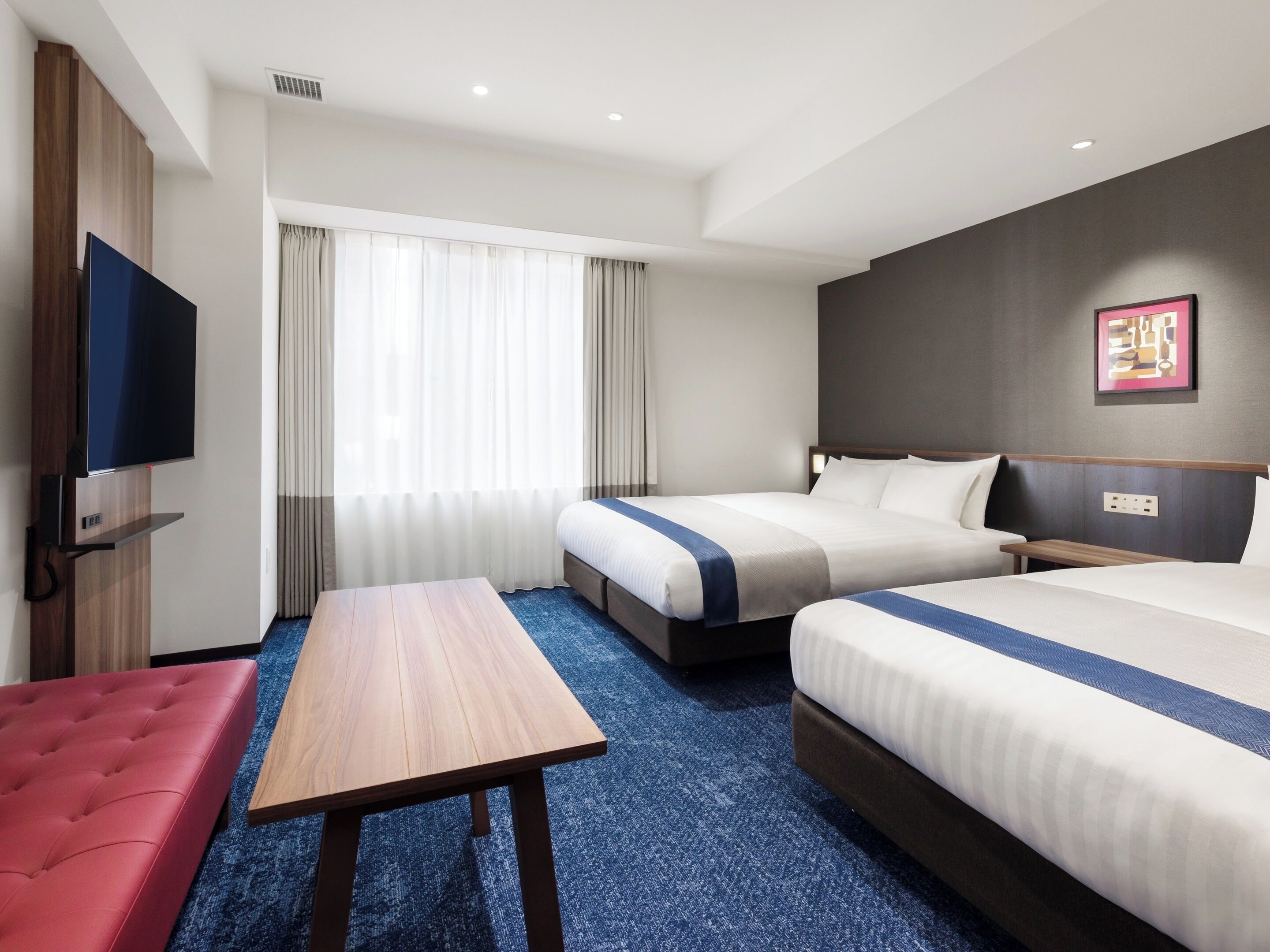Habitación de hotel con dos camas, televisión, escritorio y una banca.