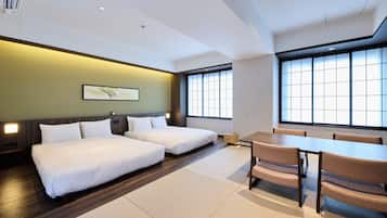 Ein Hotelzimmer mit zwei Betten, einem Esstisch, Stühlen und großen Fenstern.